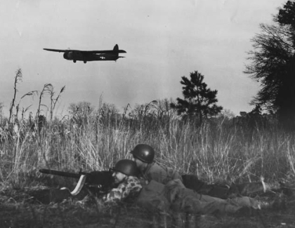 Airborne troops training at Laurinburg-Maxton Air Force Base during World War II. Image from the N.C. Museum of History Soldiers crouch in high grass while a plane flies overhead.