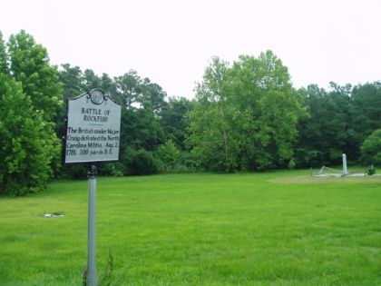 A large metallic marker in front of field circled by trees. Marker reads: "BATTLE OF ROCKFISH, The British under Major Craig defeated the North Carolina Militia, Aug. 2, 1781, 300 yards S.E."